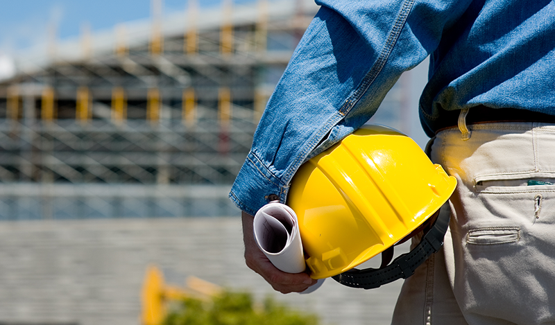 Baumeister mit Schutzhelm unter dem Arm - Rückansicht